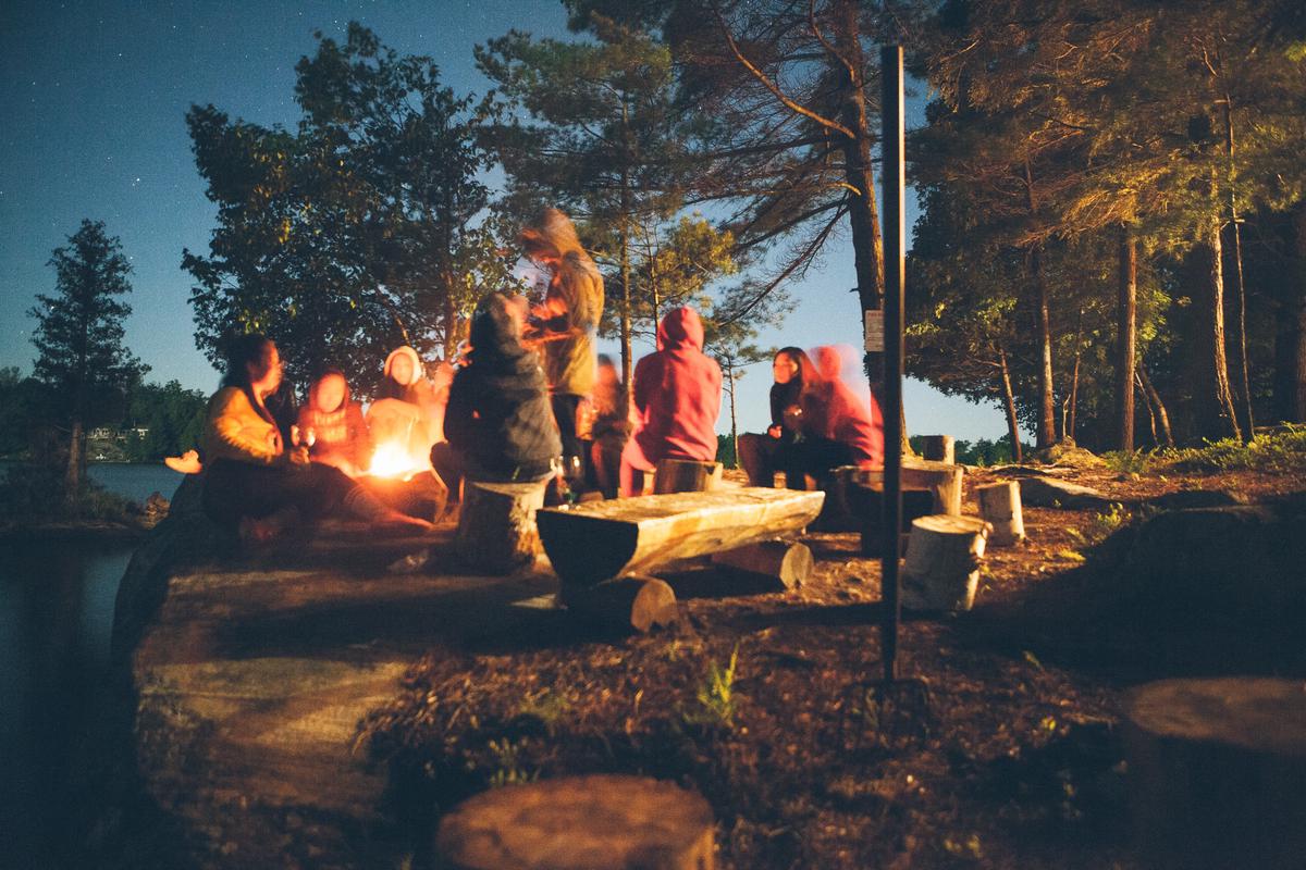 A group of campers sitting around a campfire with tents surrounded by nature